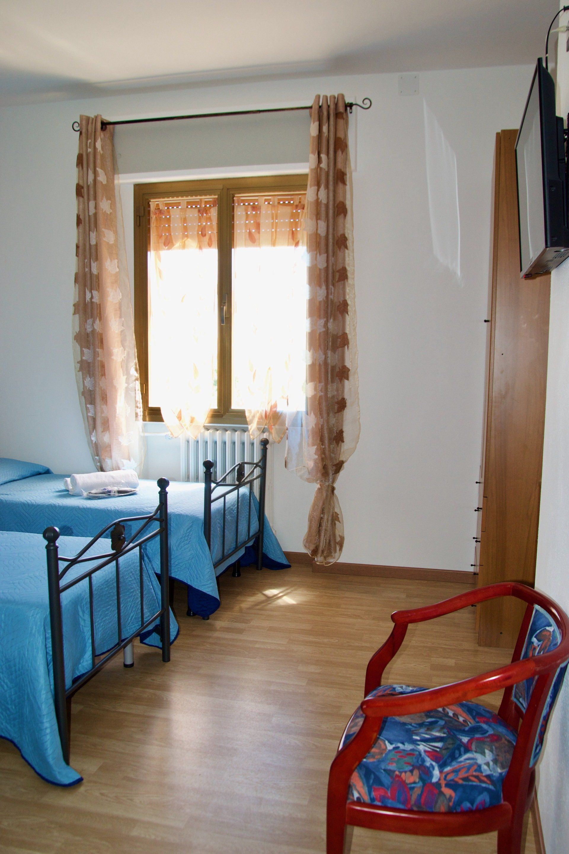 Una camera da letto con due letti e una sedia rossa in un albergo con ristorante a pochi chilometri da Bologna