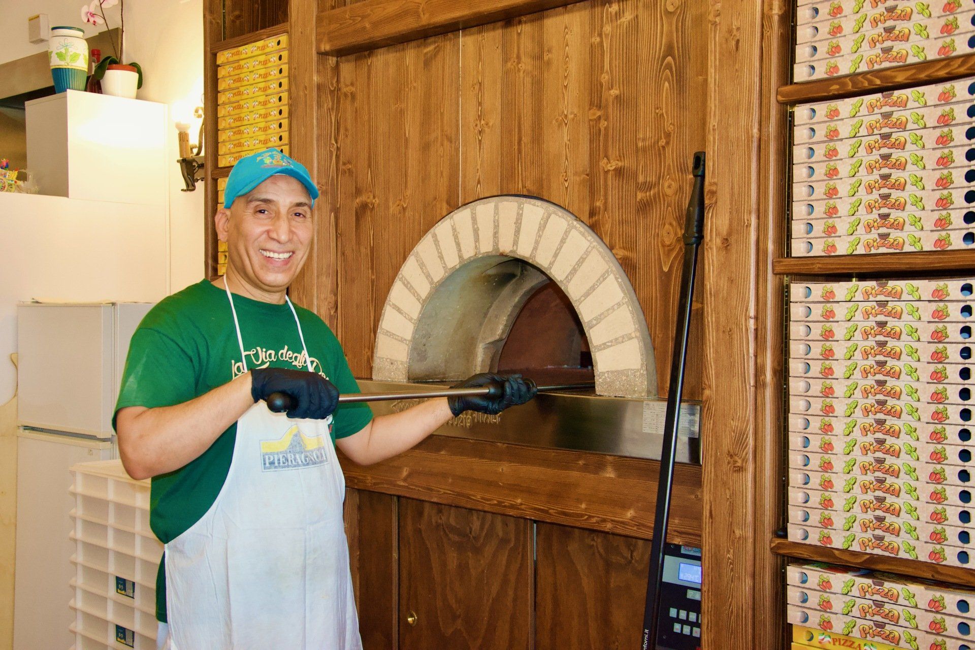 Un uomo con una camicia verde è in piedi davanti a un forno per pizza nel ristorante con specialità di funghi e tartufo a Bologna