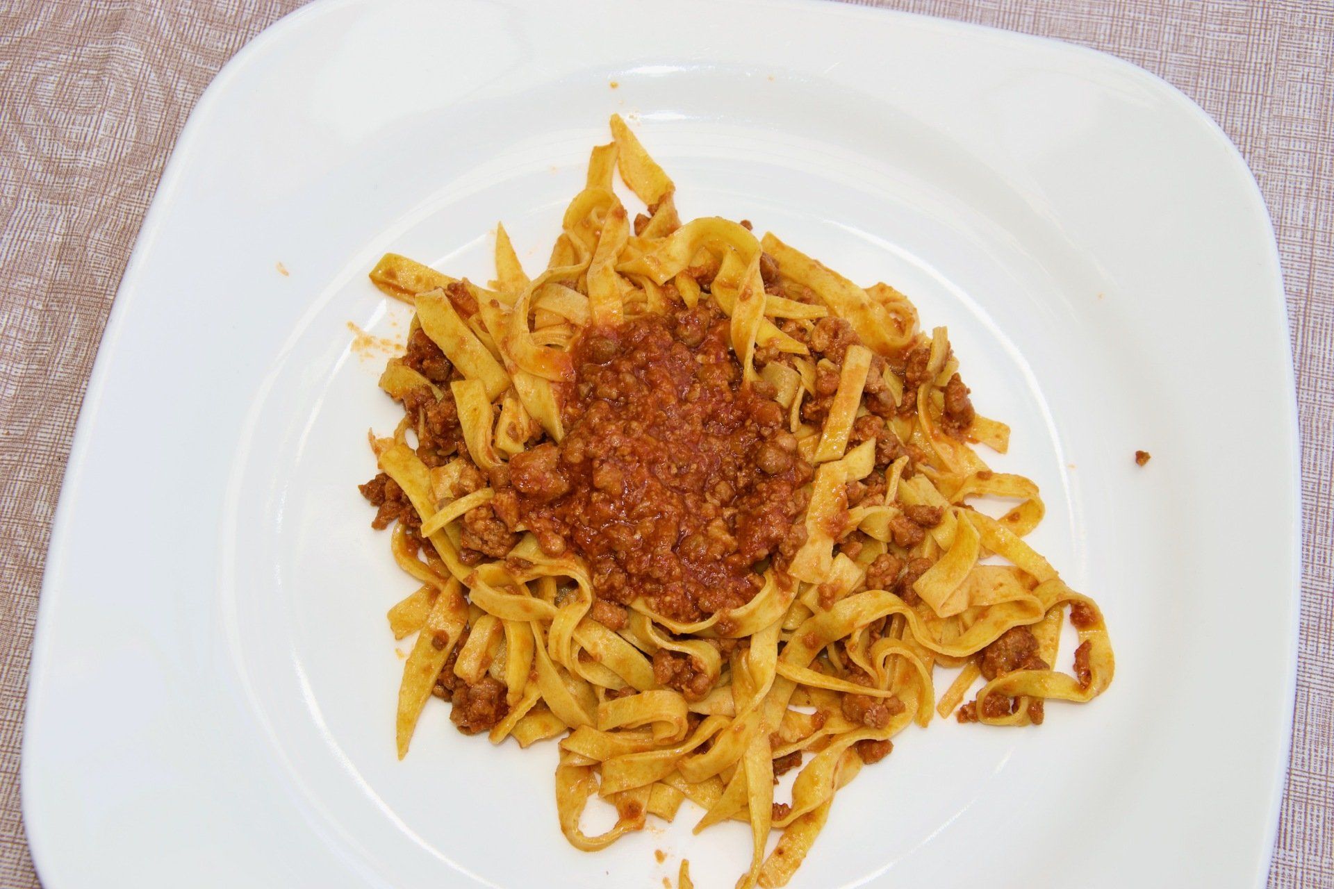 Un piatto bianco con sopra tagliatelle e sugo di carne.