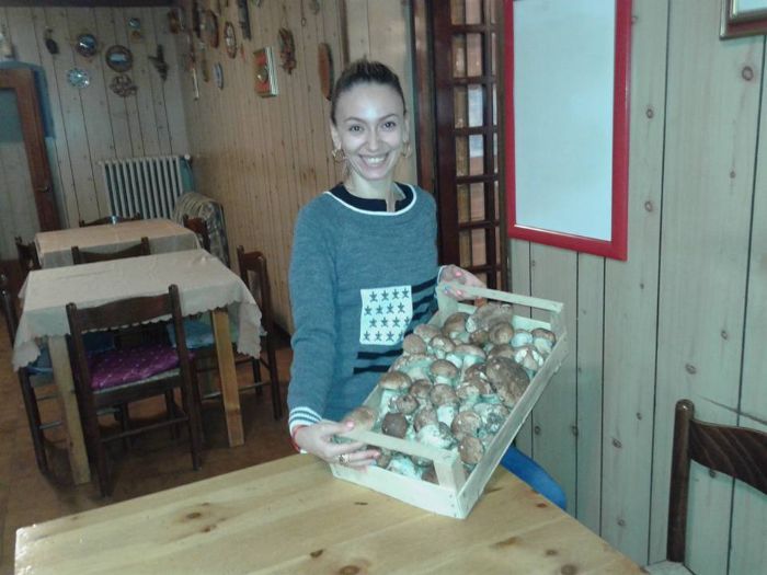 Una donna tiene in mano un vassoio di funghi su un tavolo di legno