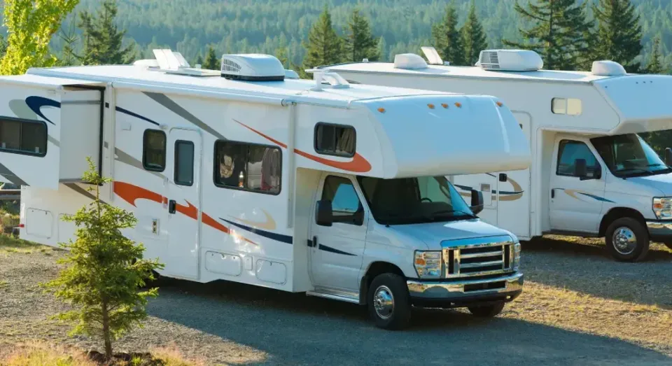 Two white rvs are parked next to each other on a gravel road.