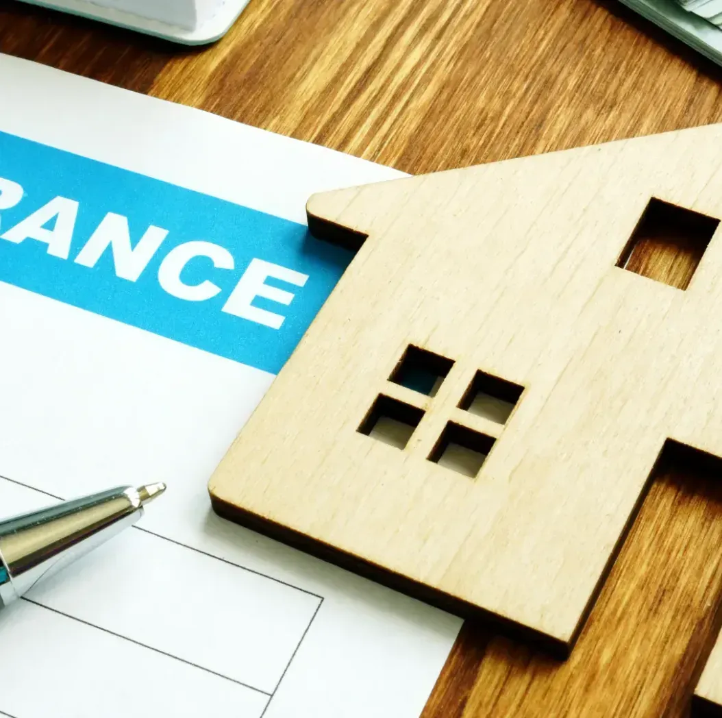 A wooden house is sitting on top of a piece of paper that says insurance.