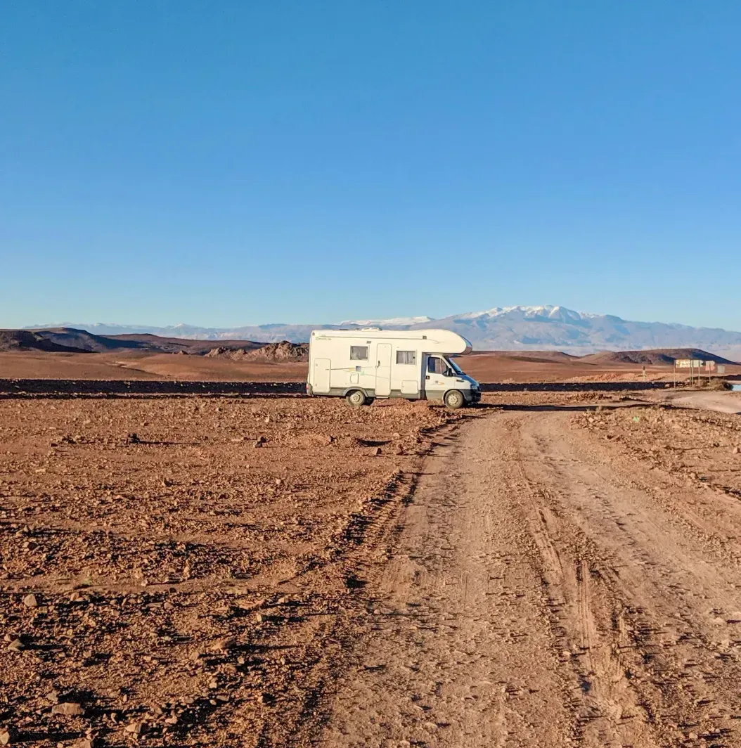 A rv is parked on the side of a dirt road in the desert.