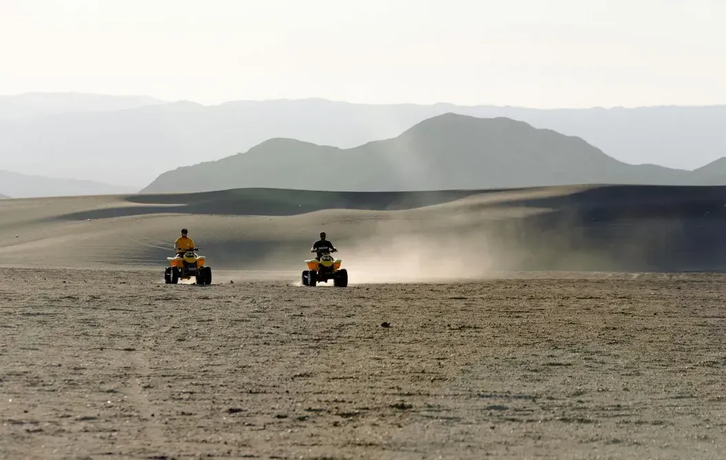 Two people are riding atvs in the desert.