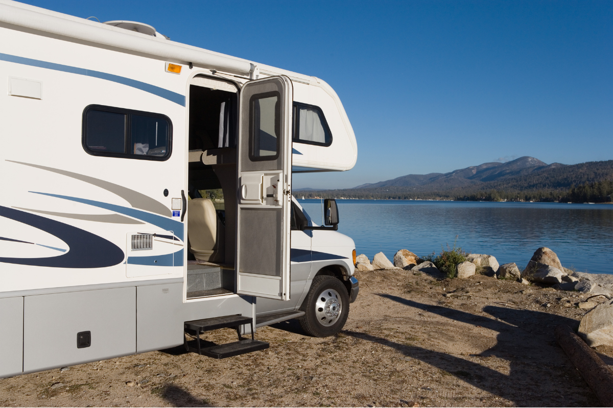 A white rv is parked next to a lake with the door open.