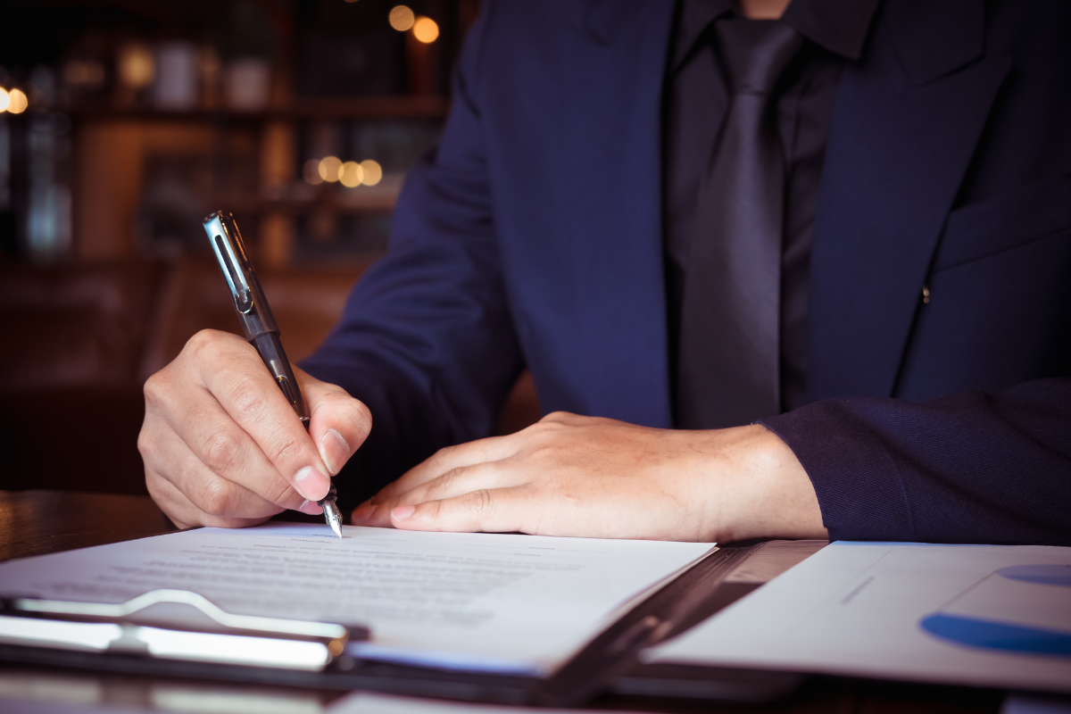A man in a suit and tie is signing a document with a pen.