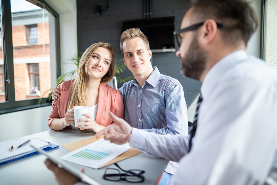 A man and a woman are sitting at a table talking to an insurance agent.