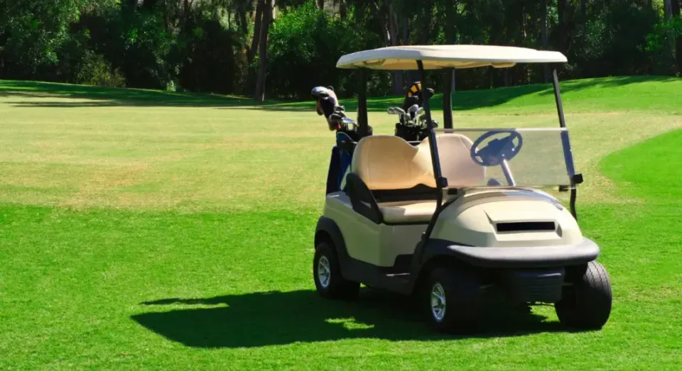A golf cart is parked on the grass on a golf course.