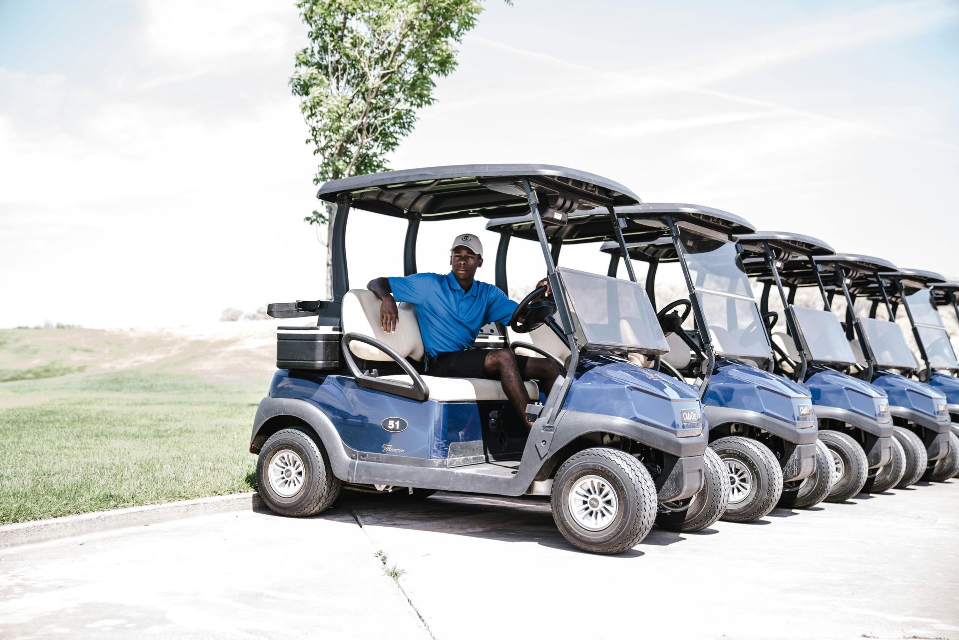 A man is sitting in a golf cart next to a row of golf carts.