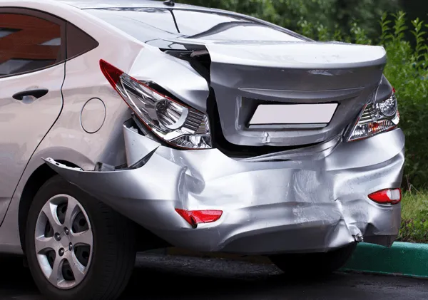 A silver sedan with severe rear-end damage, including a crumpled bumper and a misaligned, dented trunk lid.