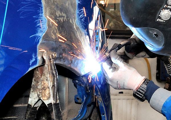 A man wearing a welding helmet is welding a blue car
