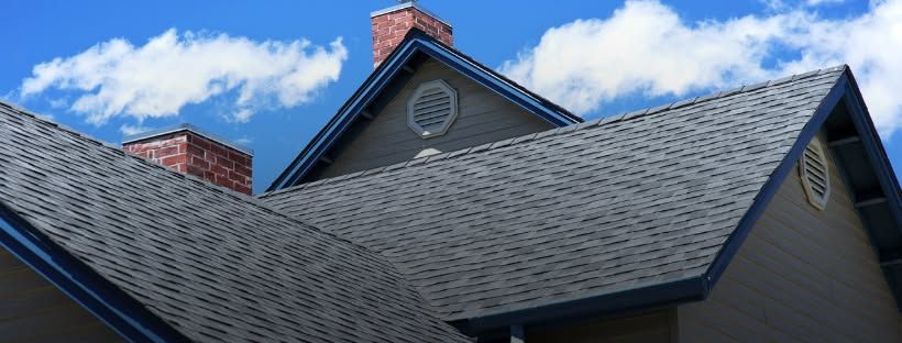 A house with a roof and chimneys against a blue sky with clouds.