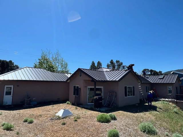 A man is standing in front of a house with a metal roof.