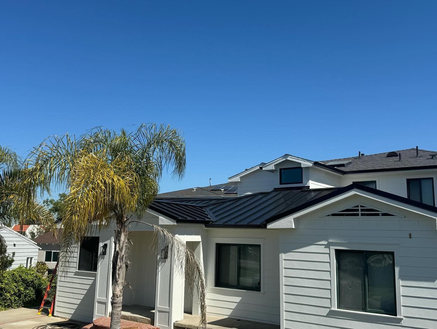 A white house with a black roof and a palm tree in front of it.