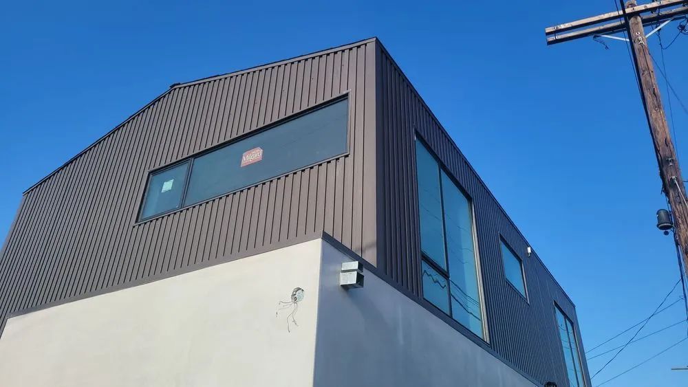 Modern gray building with ribbed siding and large windows against a blue sky.
