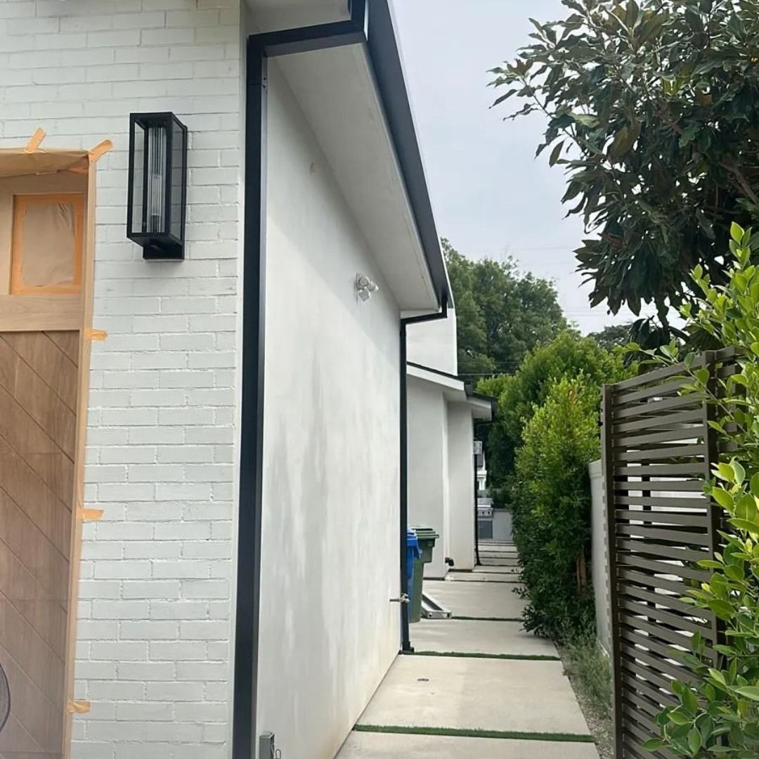 A white brick house with a black gutter on the side of it.