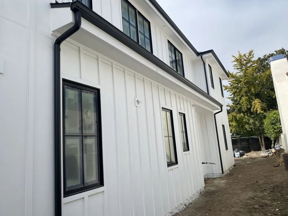 White house with black window frames, gutters. Vertical siding. Exterior.