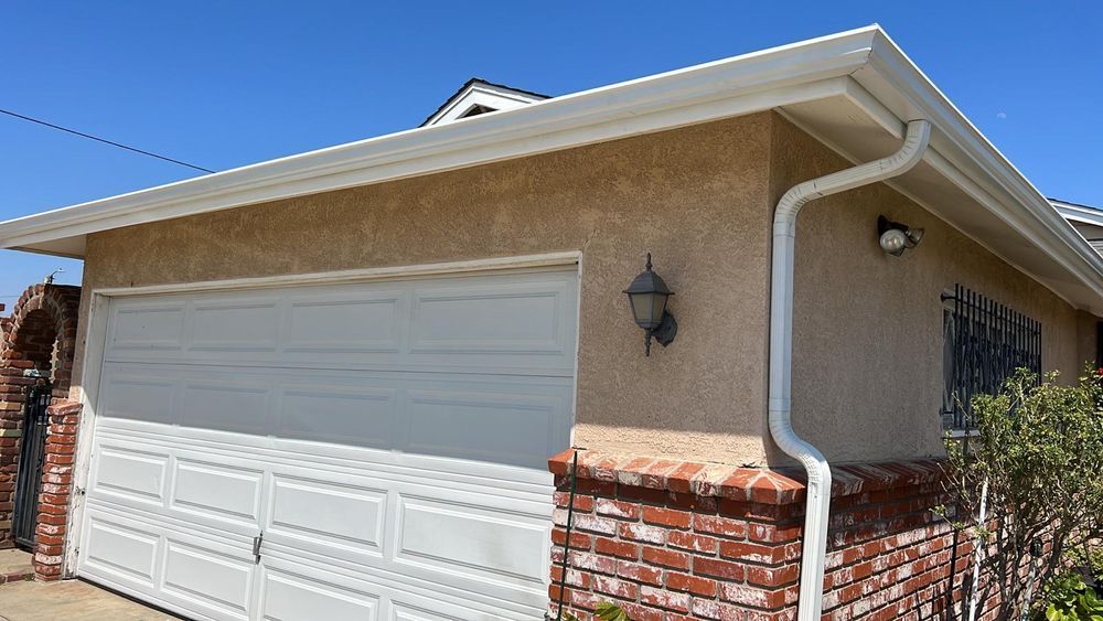 A garage with a white door and a white gutter on the side of a house.