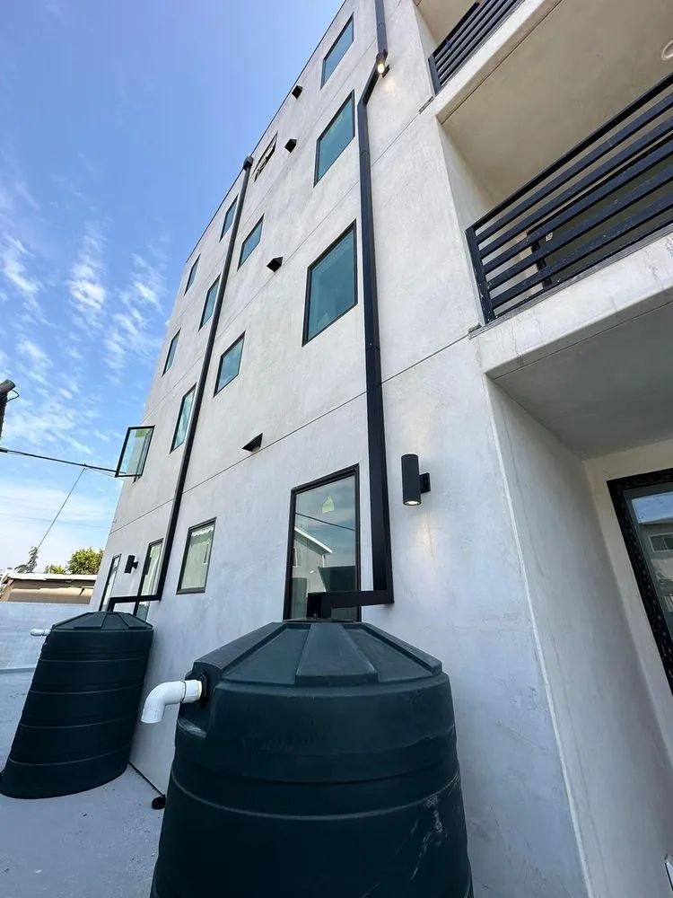 Two large, dark green water tanks sit at the base of a modern white building with black downspouts and windows.