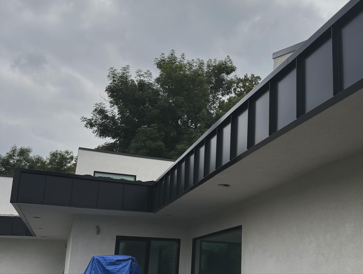 A white house with a black roof and a blue tarp in front of it