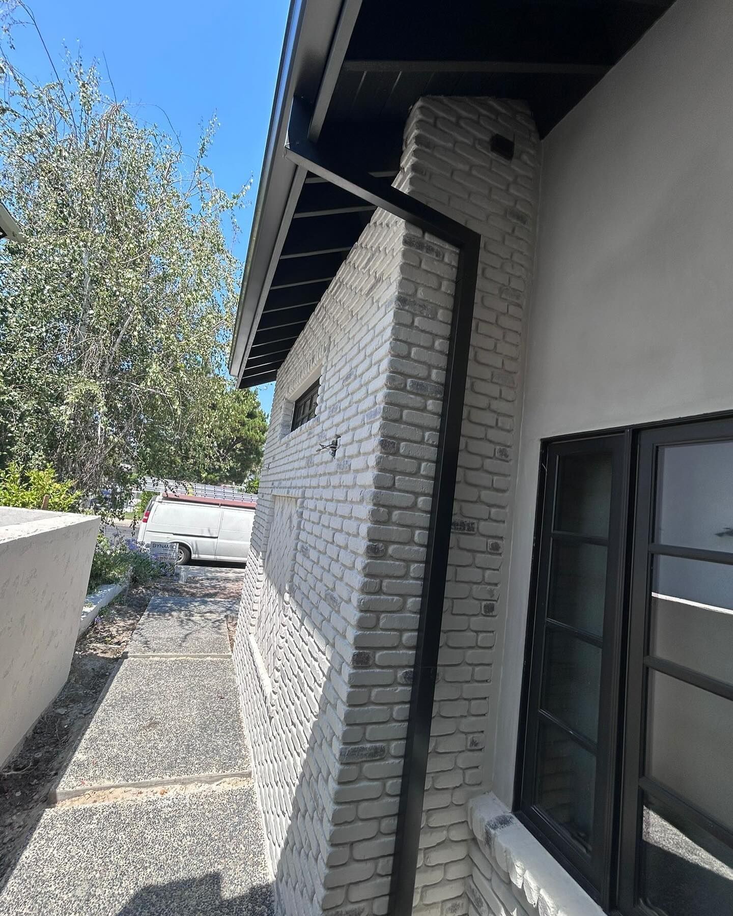 A white brick building with a black gutter on the side of it.
