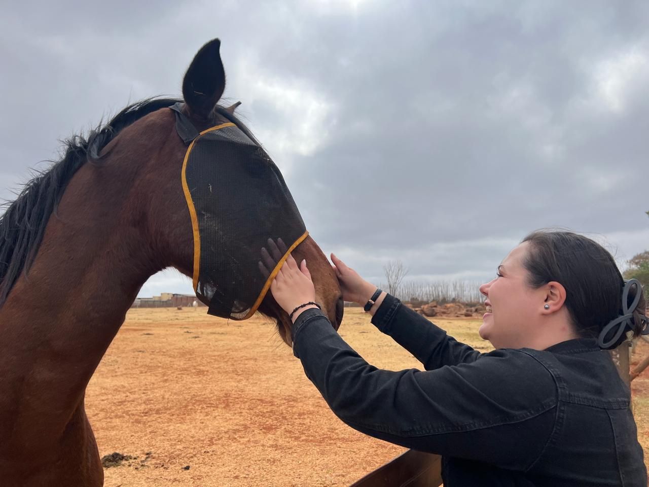 A woman is petting a brown horse wearing a mask.