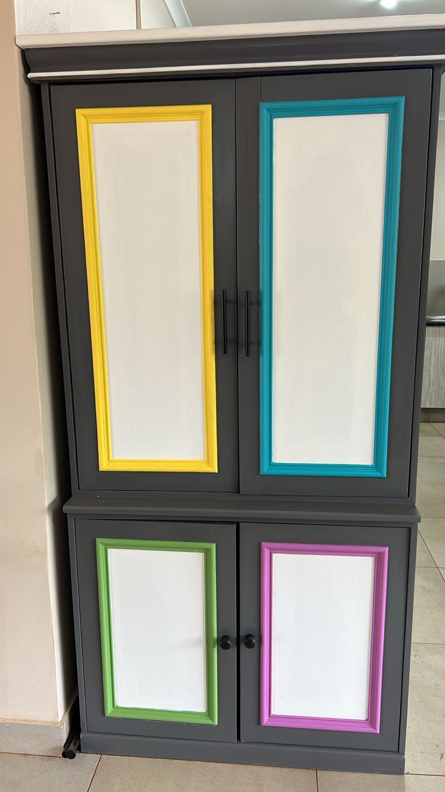 A gray cabinet with colorful trim is sitting on a tiled floor.