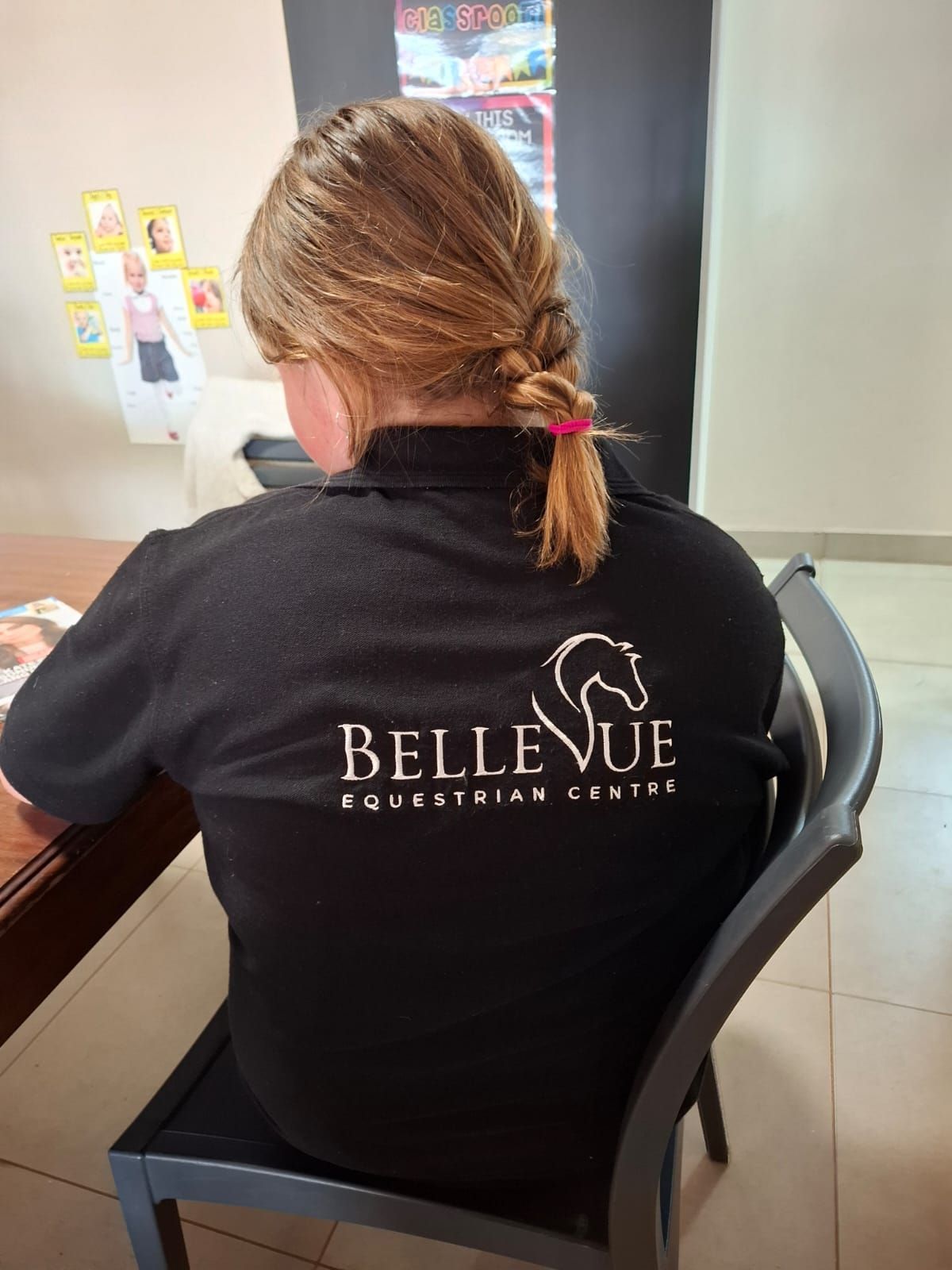 A woman is sitting in a chair wearing a black bellevue polo shirt.