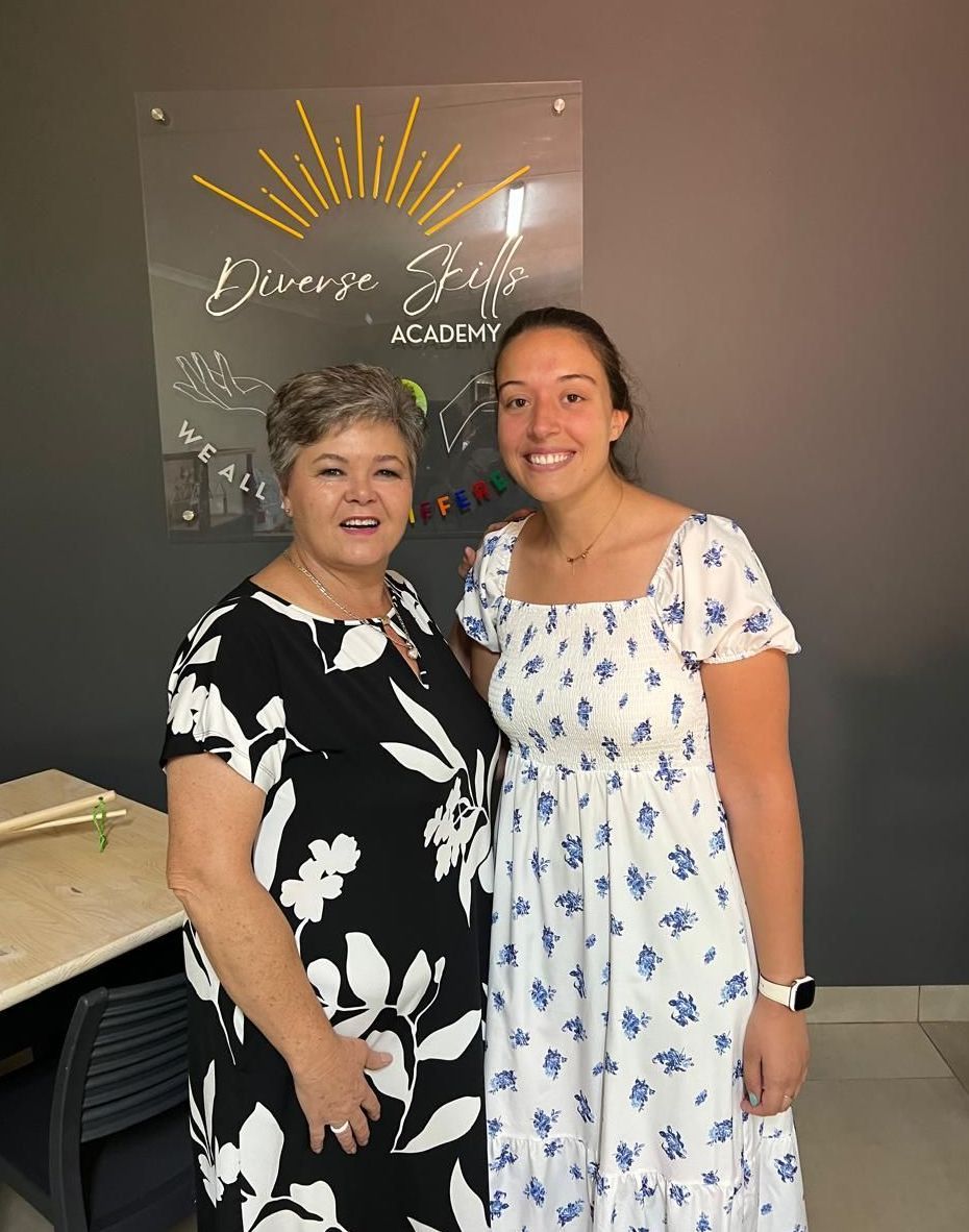 Two women are posing for a picture in front of a sign.