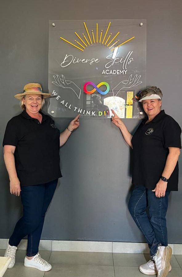 Two women are standing next to each other in front of a sign.