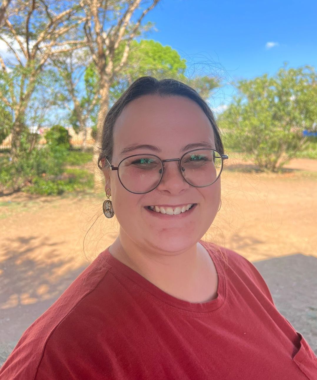 A woman wearing glasses and a red shirt is smiling for the camera.