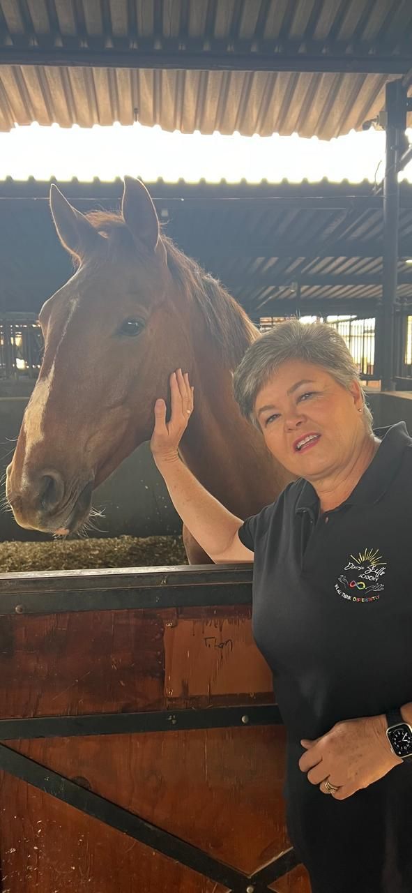 The owner of Diverse Skills Academy is petting a brown horse in a stable.