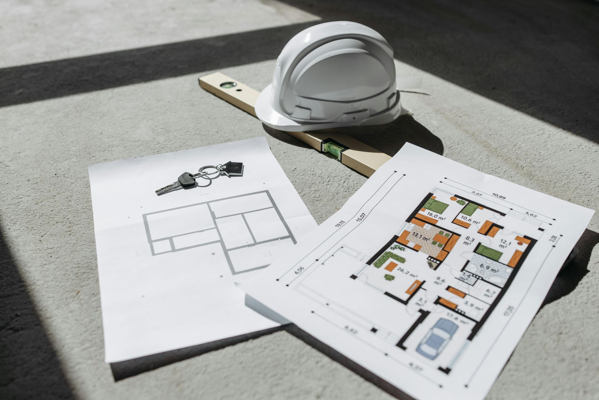Architectural blueprints and a white hard hat on a concrete surface, indicating construction planning.