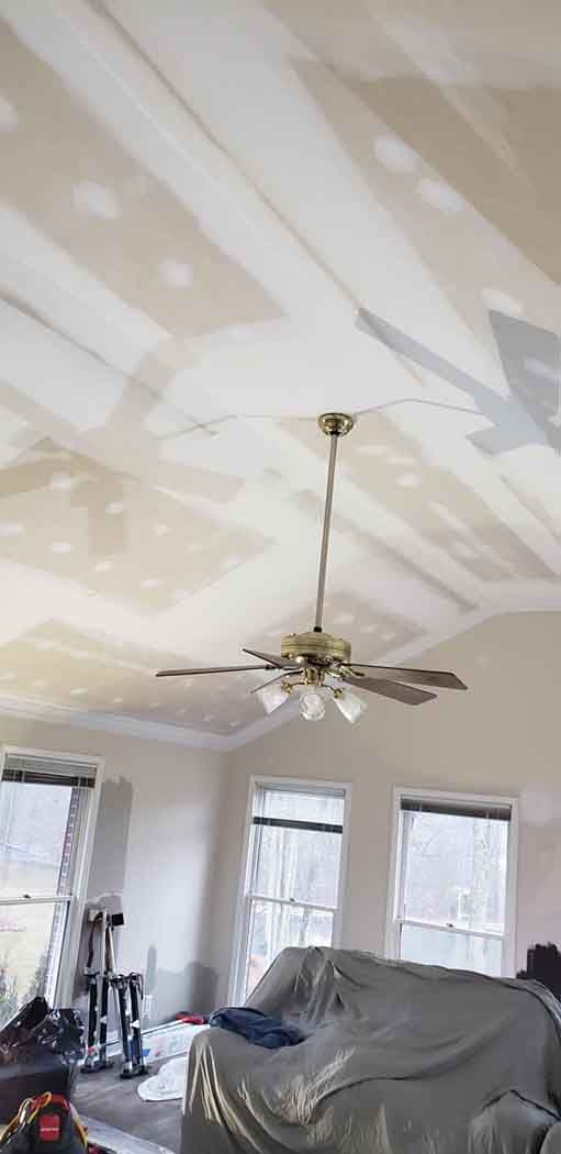 Ceiling with a ceiling fan, three windows, and covered furniture.