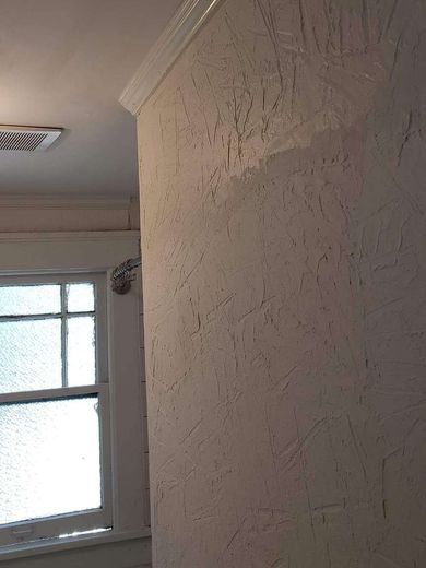 Corner of a room with textured white wall, window, and crown molding.