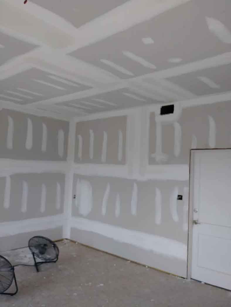 Interior room with drywall installation, including walls, ceiling, and door. Fans placed on floor.