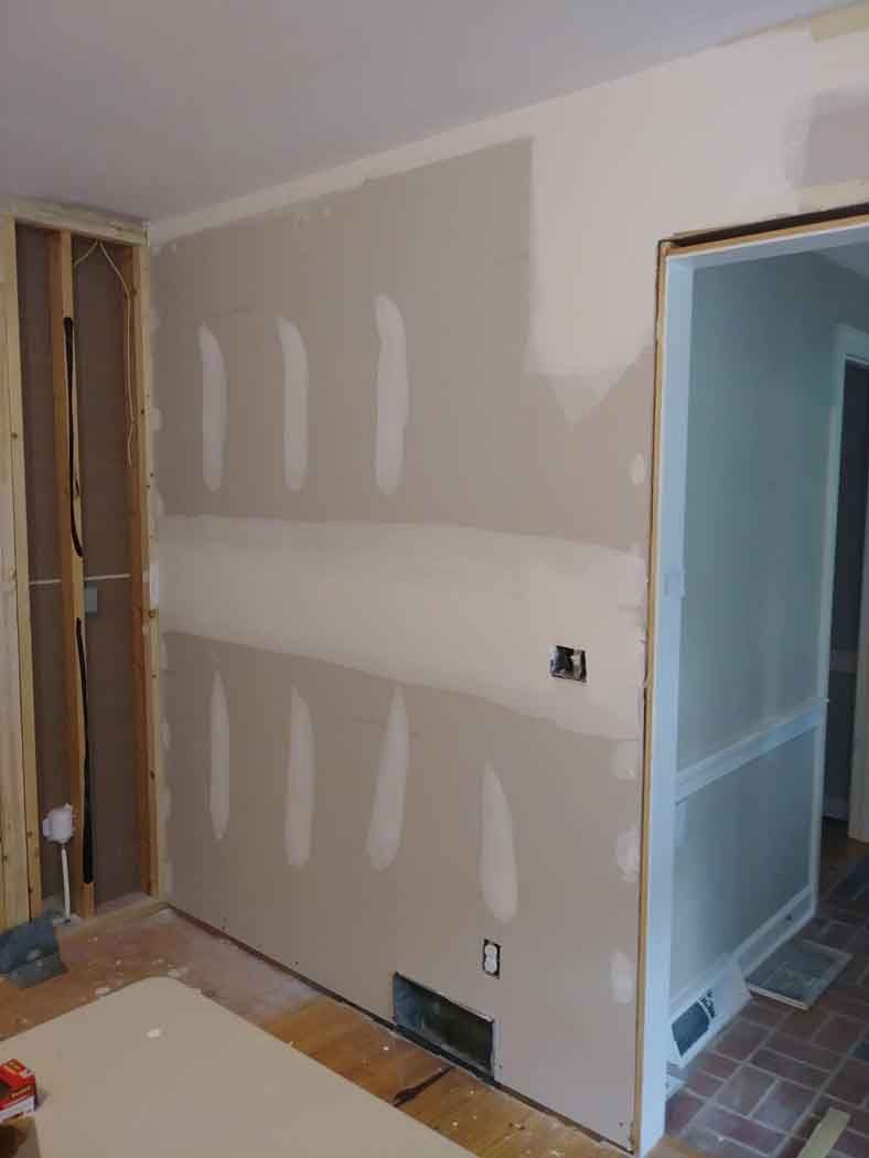 Drywall installation in progress; interior wall with taped seams, electrical outlets, and a doorway.