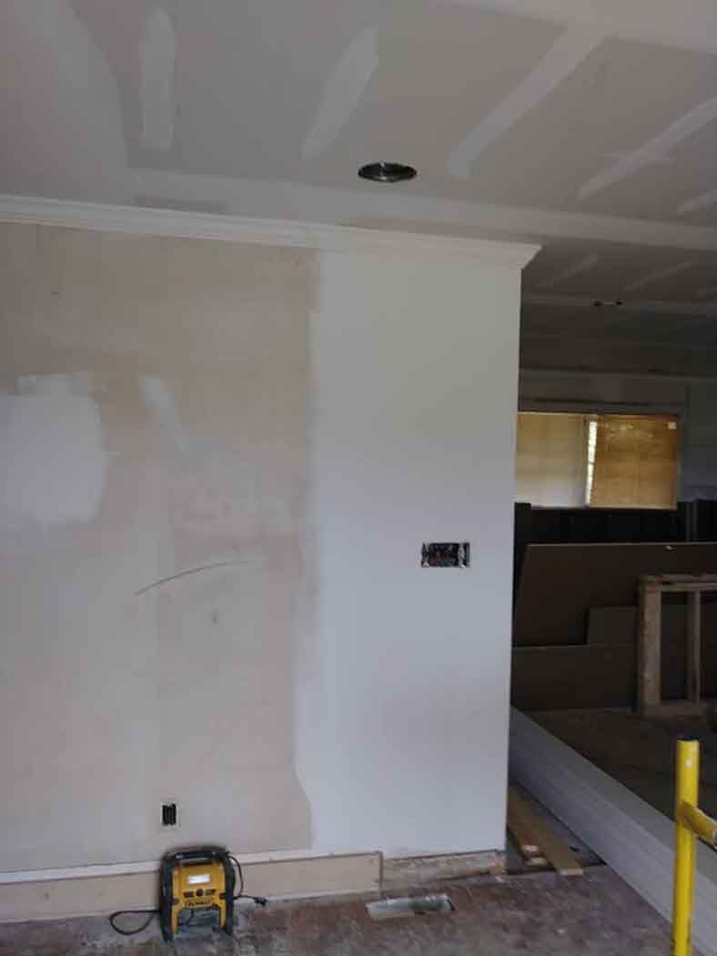 Interior wall under construction, partially painted, with crown molding. Light switch and electrical box visible.
