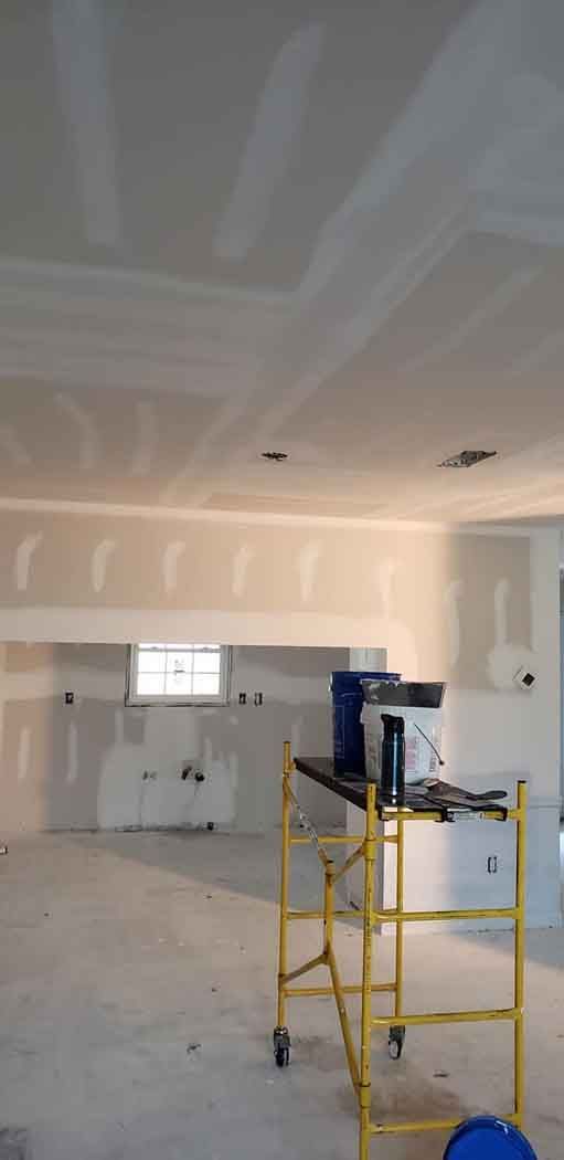 Interior view of a room under construction with scaffolding, drywall, and a window.