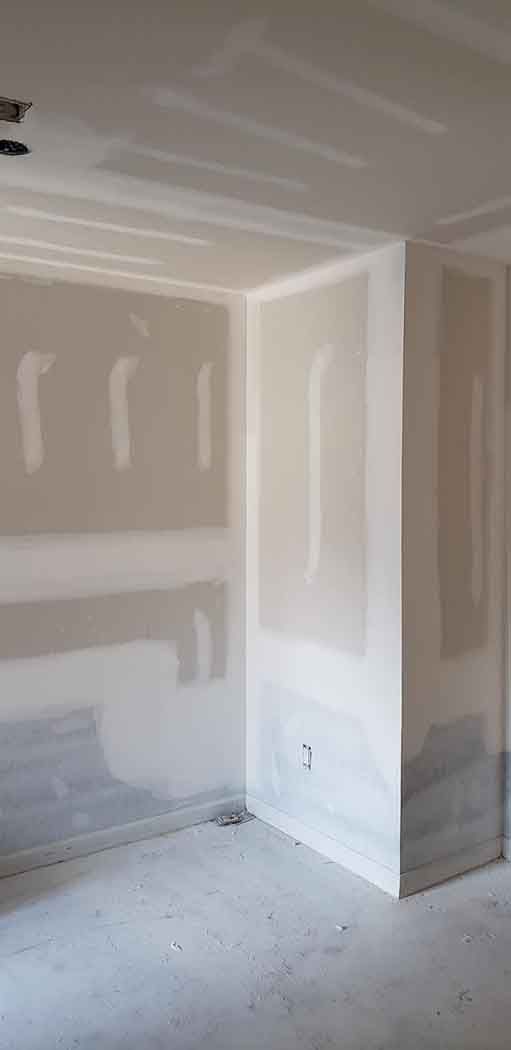 Interior corner of a room under construction with drywall and unfinished floor.