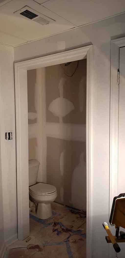 A doorway opening into a small bathroom with a toilet. Walls are unfinished, and debris is on the floor.