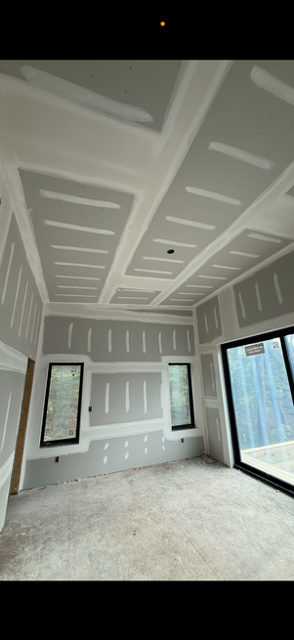 Interior room under construction, with drywall walls and ceiling, window, and sliding glass door.