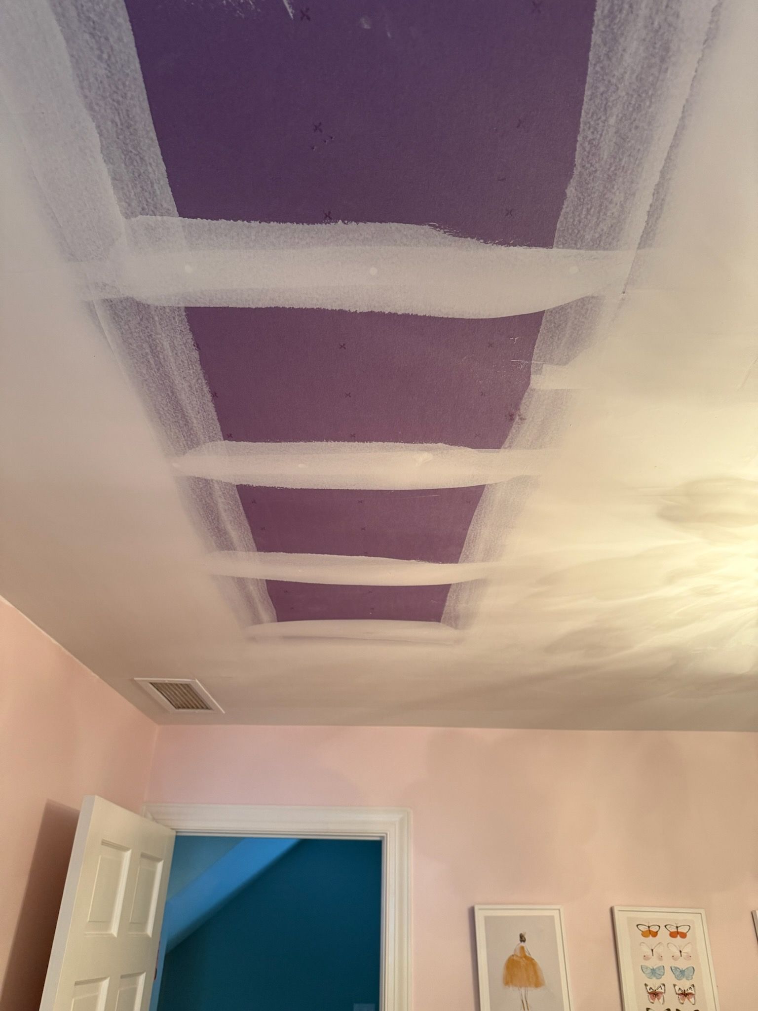 Unfinished room with drywall walls and ceiling, taped seams, and a white door. A fan sits on the floor.