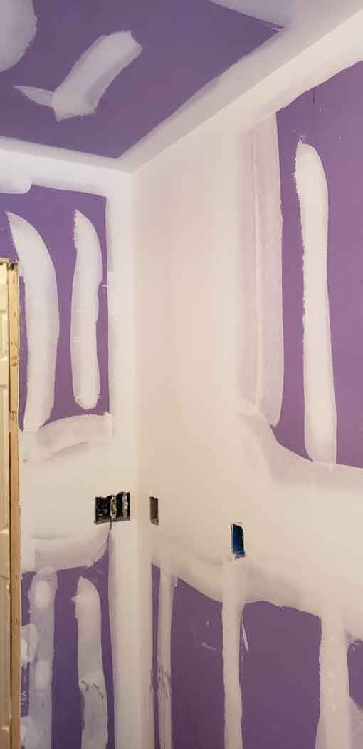 Interior view of a room under construction with purple drywall and white joint compound.