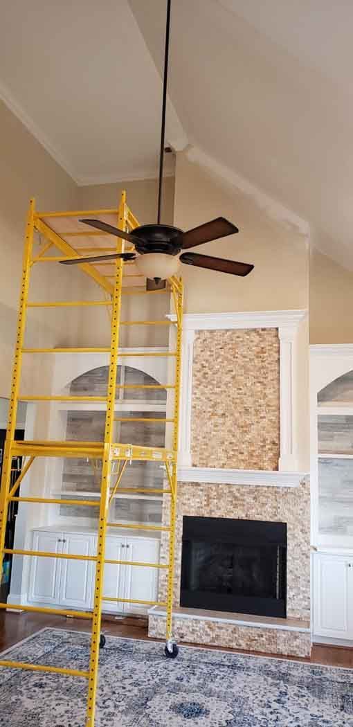 A room with a fireplace, ceiling fan, scaffolding, and built-in shelving.