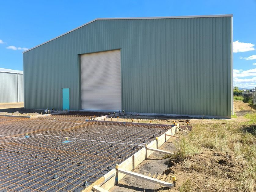 A Green Metal Building With A White Garage Door Is Being Built — B & C Donnachie Concrete Contractors in Atherton, QLD