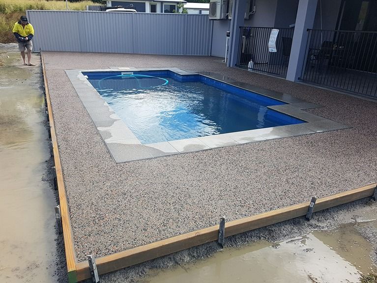 A Man Is Standing Next To A Swimming Pool In A Backyard — B & C Donnachie Concrete Contractors in Smithfield, QLD