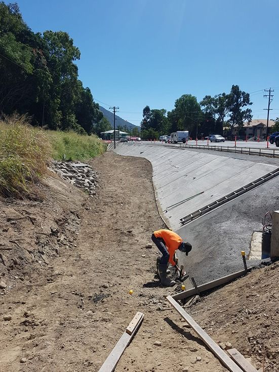 A Man Is Kneeling Down In The Dirt Next To A Road — B & C Donnachie Concrete Contractors in Kuranda, QLD