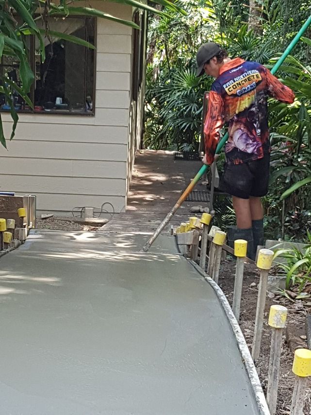 A Man Is Spreading Concrete On A Sidewalk With A Broom — B & C Donnachie Concrete Contractors in Kuranda, QLD