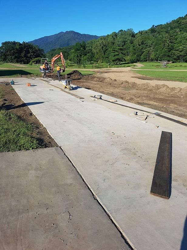 A Concrete Walkway Is Being Built In A Field With Mountains In The Background — B & C Donnachie Concrete Contractors in Smithfield, QLD